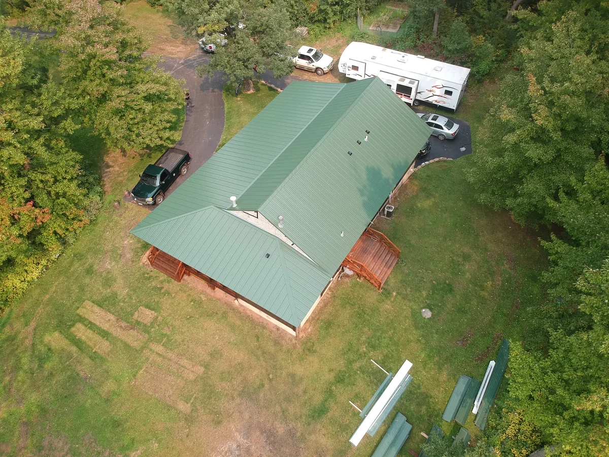 Overhead view of the green metal roof with a camper parked beside the home in early autumn.
