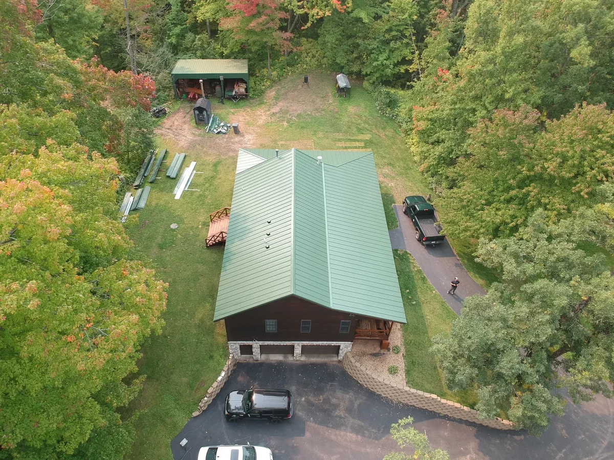Angled view of the green metal roof on the log home with a matching outbuilding and driveway.