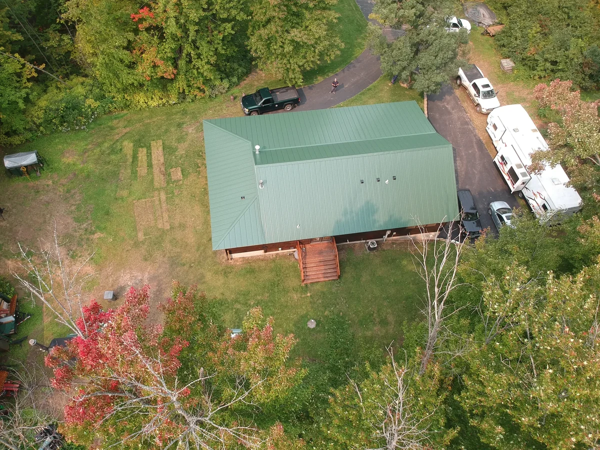 Aerial of the green roof with a camper and vehicles set in the shaded clearing.