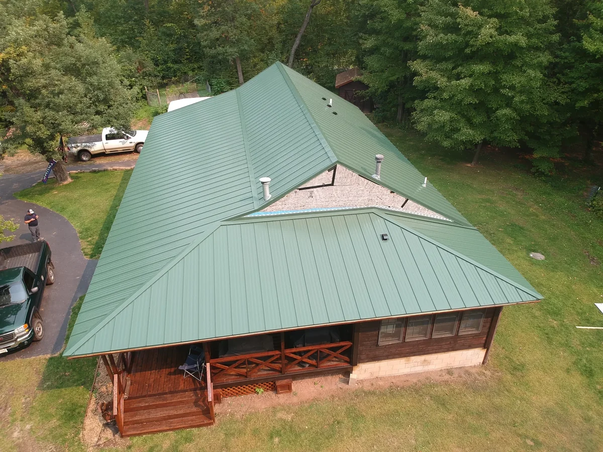 Low front angle of the green hip roof crowning the log home.