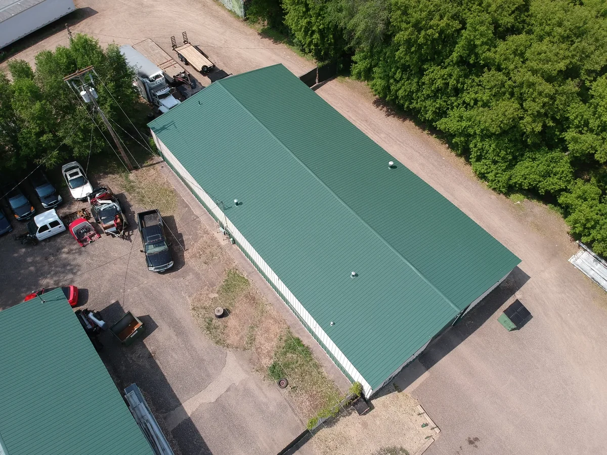 Drone shot of the long green metal roof running the length of the warehouse beside the parking lot