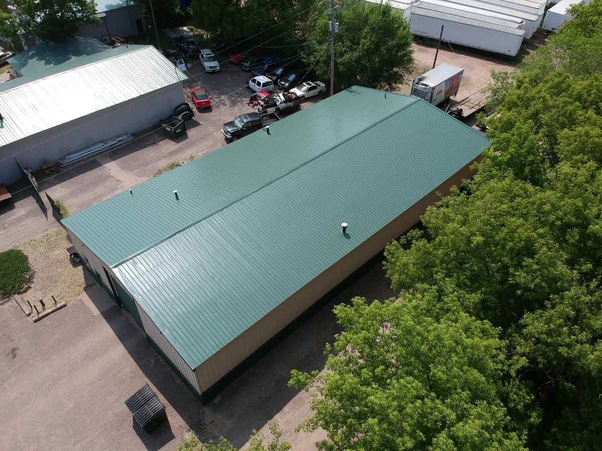 Angled aerial of the green metal roof with vehicles and outbuildings nearby