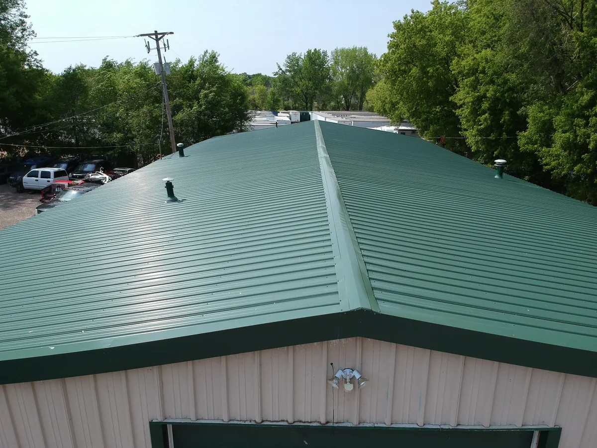 Close aerial of the green metal roof ridge and panels above the building's tan walls