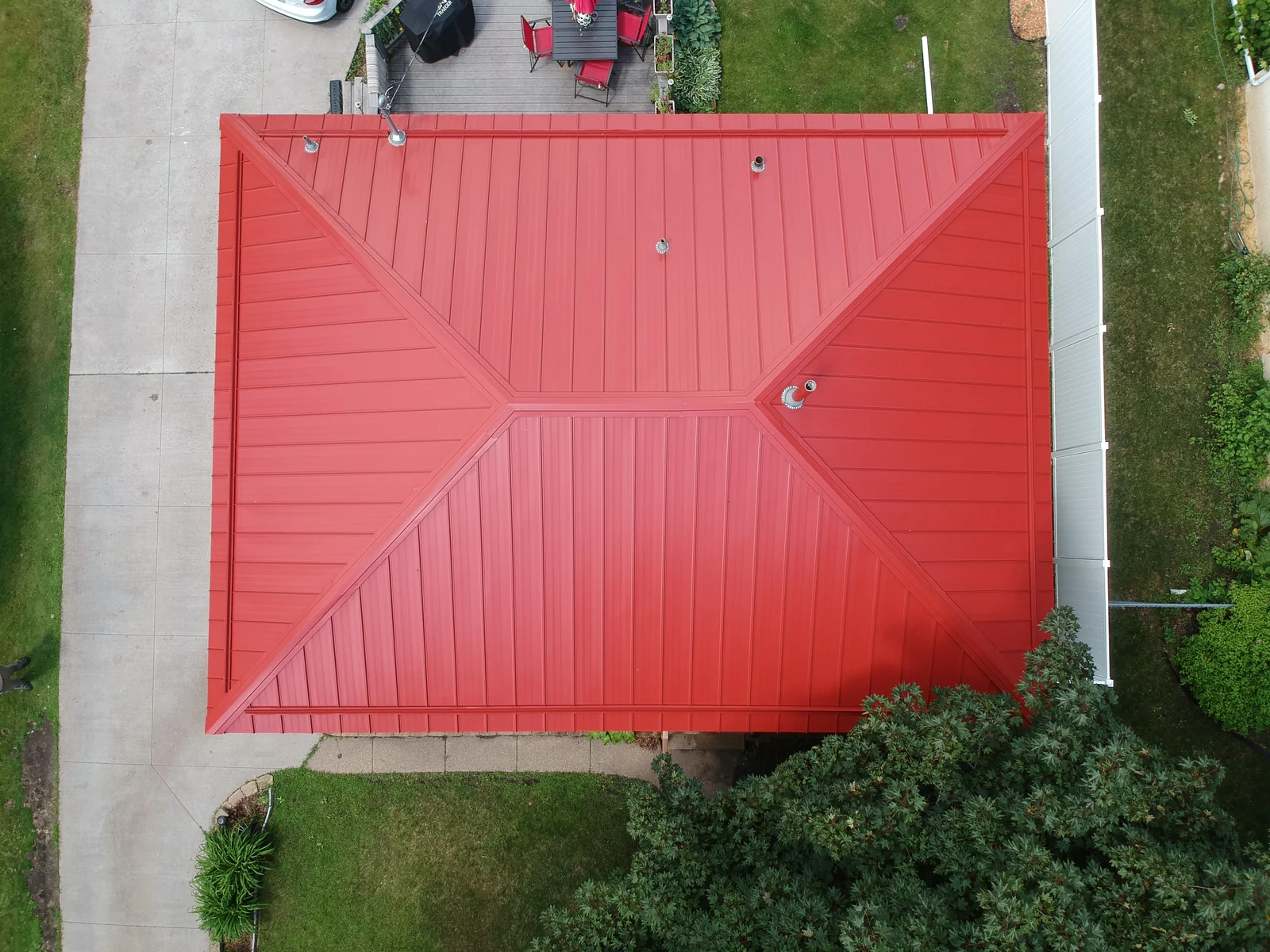 Top-down view of the bright red hipped standing seam roof and surrounding pavement.