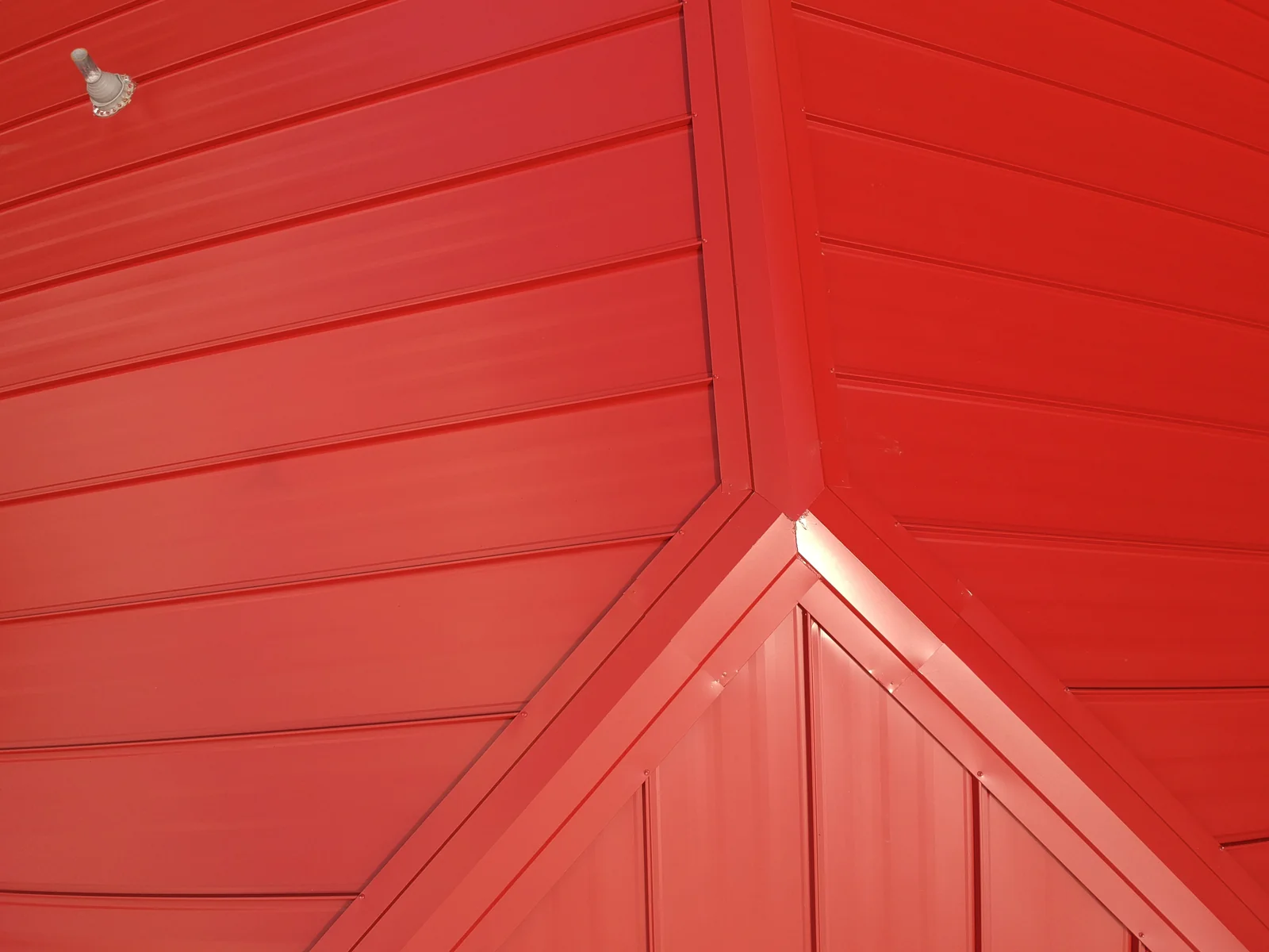 Close detail of the red standing seam panels converging at the roof hip and ridge.