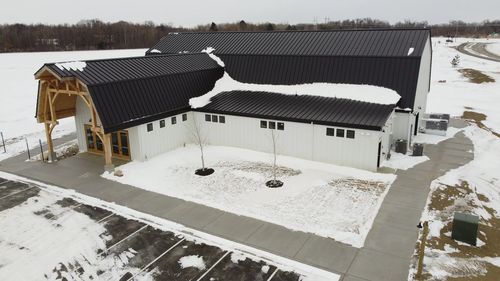 Aerial view of a dark metal roof on a timber-accented commercial building in St. Cloud, MN, with a snowy parking lot.