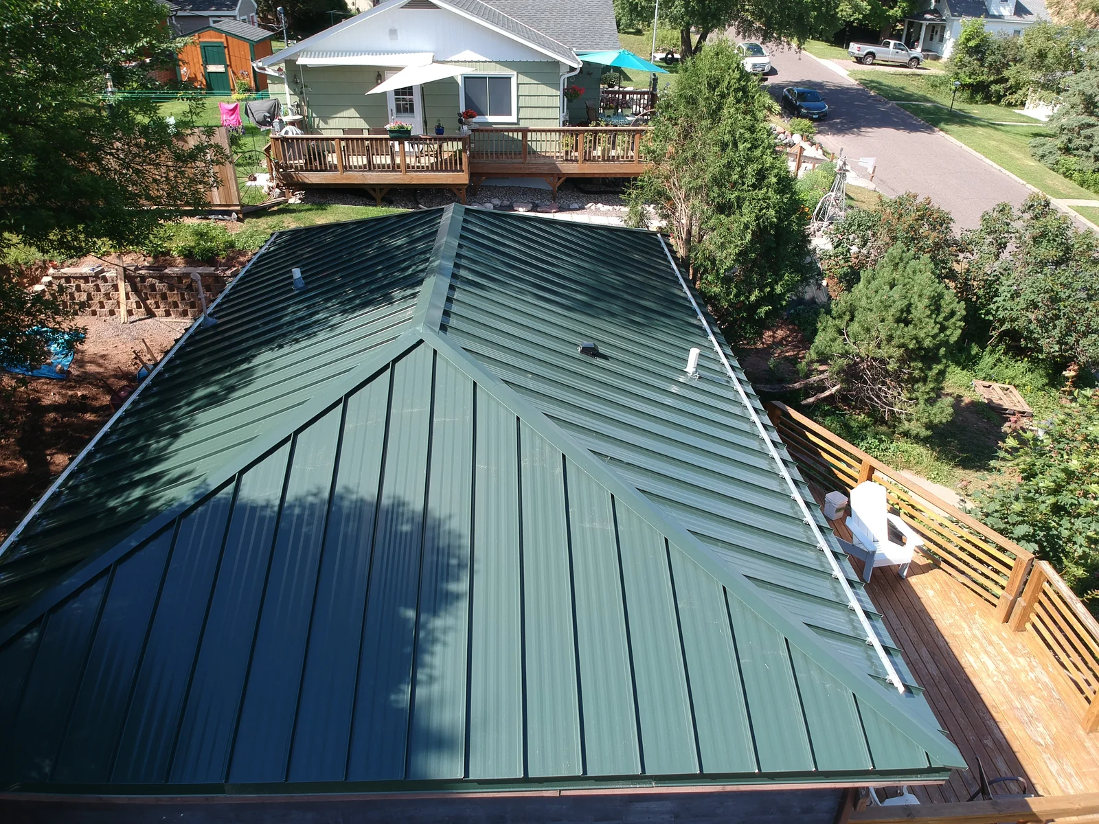 Low-angle drone shot of the green metal roof with the residential street beyond