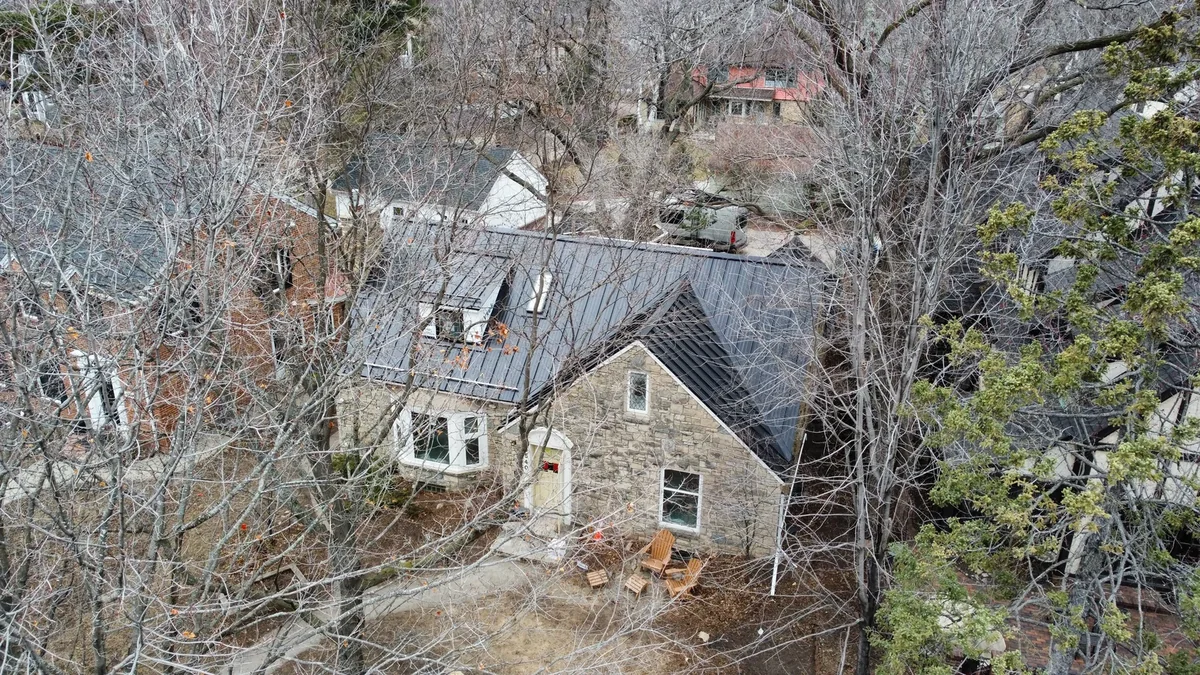 Drone shot of the grey metal roof over the historic stone home and its wooded lot