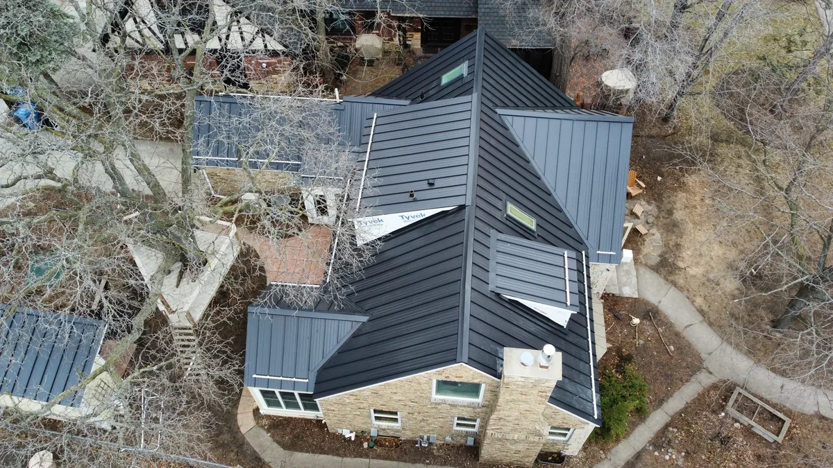 Top-down view of the grey standing seam roof and the home's stone chimney