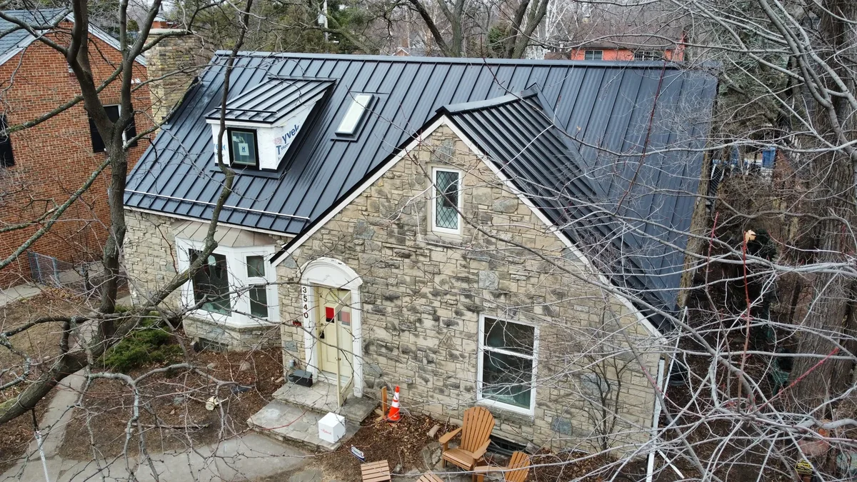 Drone view of the grey-roofed stone house framed by neighboring trees