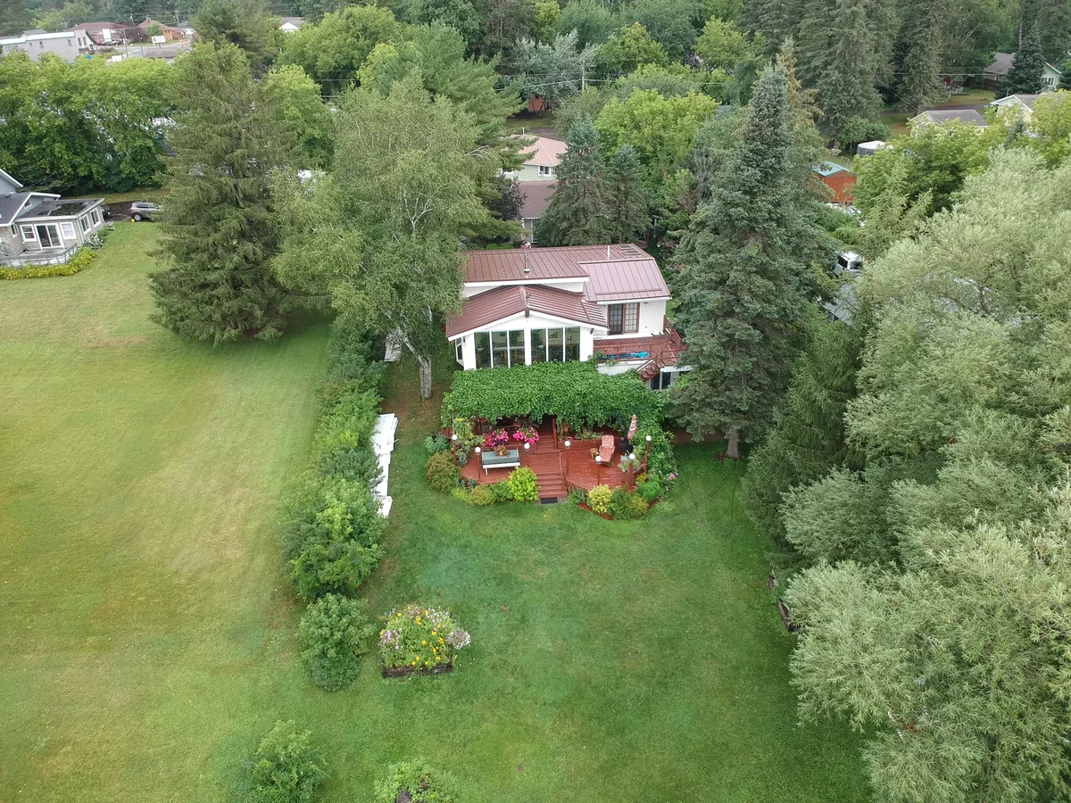 Drone shot of the home framed by green trees with the brown roof in full sun.