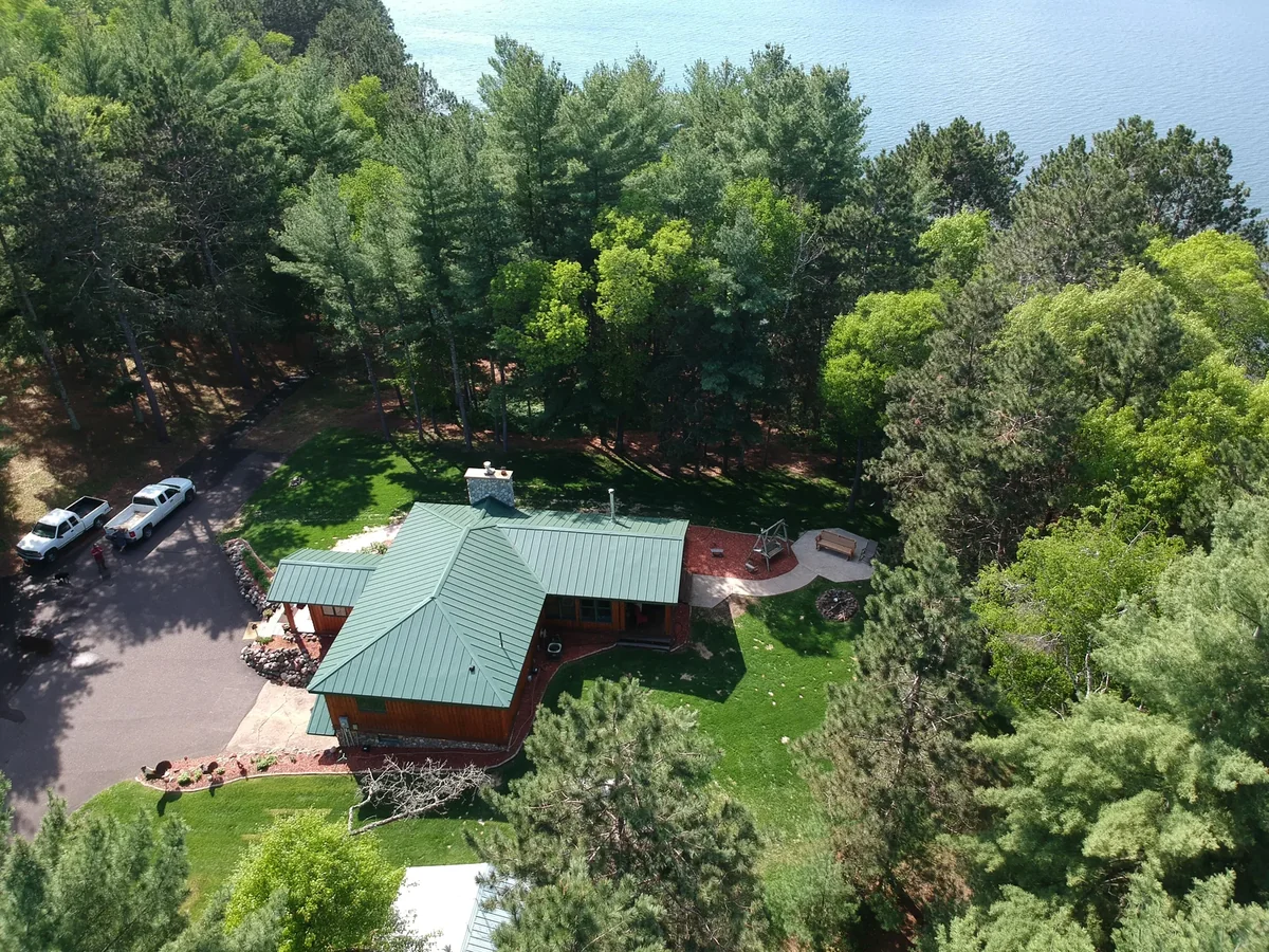 Angled aerial of the green-roofed home framed by dense surrounding forest.