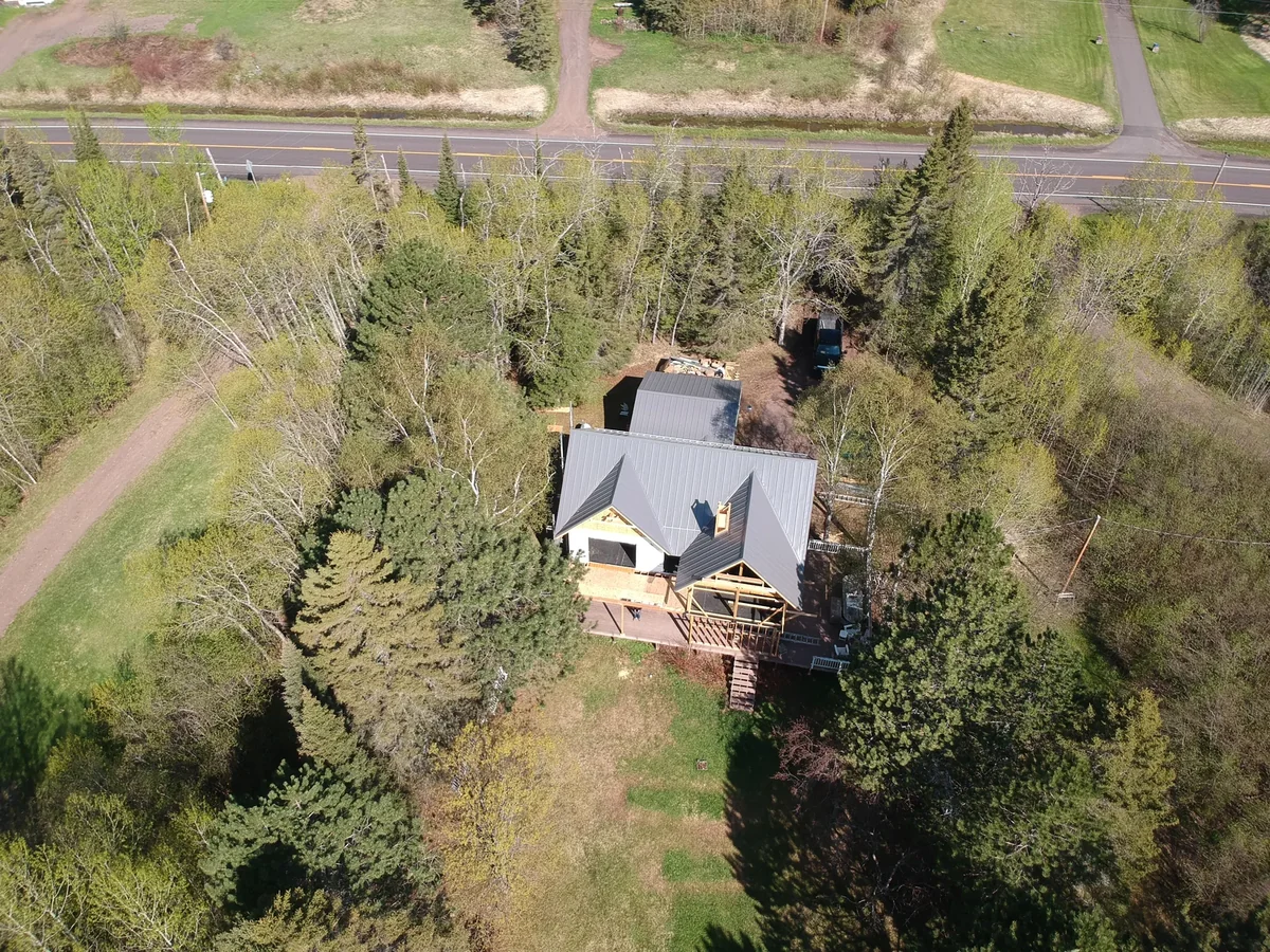 Drone shot of the home with its grey metal roof tucked among tall pines beside the highway