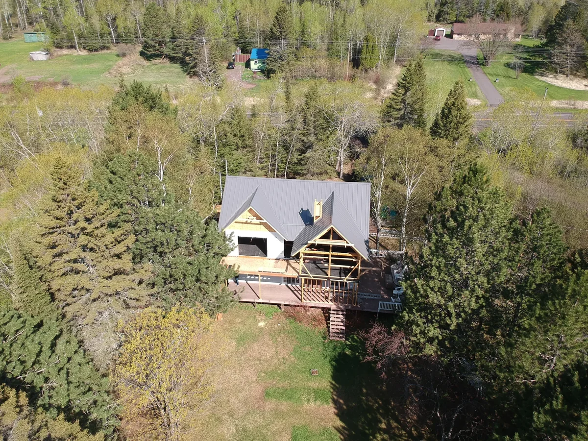 Aerial of the grey metal roof home set in a clearing surrounded by evergreens