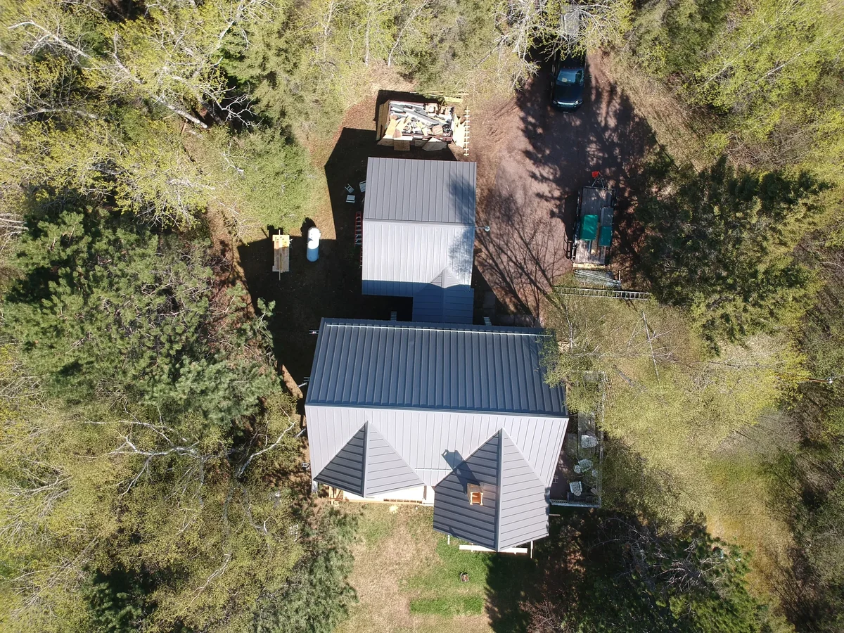 Overhead view of the grey metal roof and a detached structure among the wooded lot