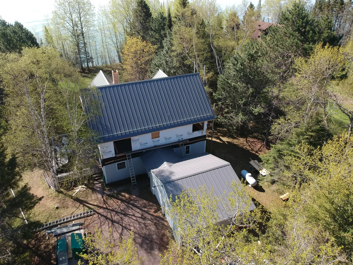 Close aerial of the two-story home and its grey metal roof framed by spring trees