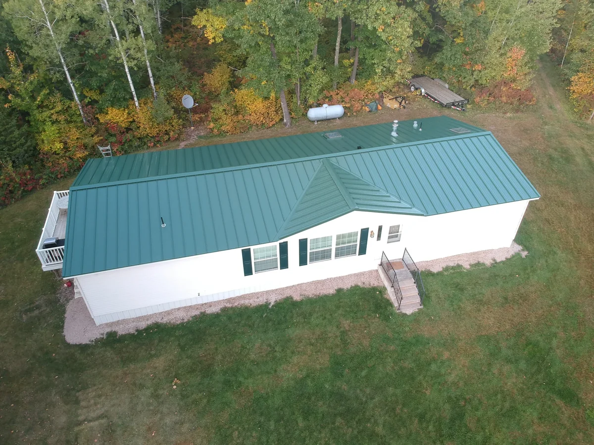 Aerial view of a long ranch home with a forest-green standing seam metal roof in Virginia, MN.
