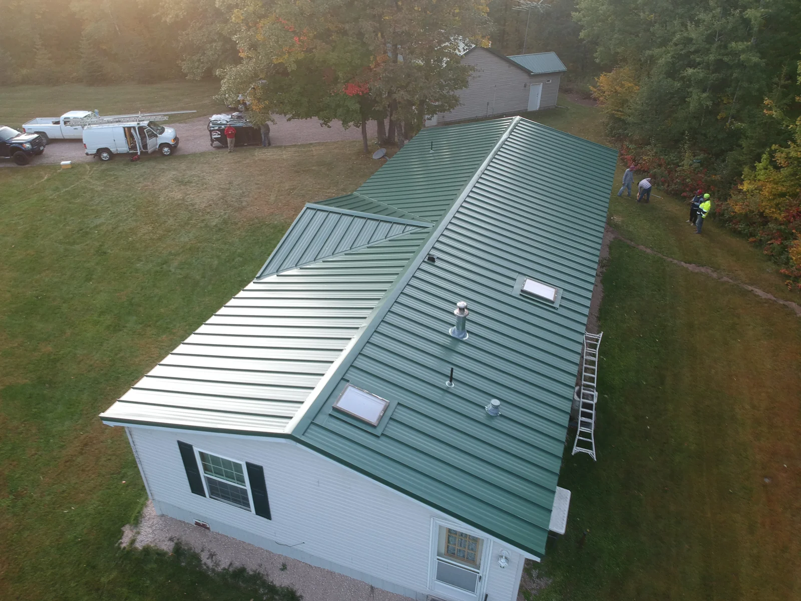 Drone shot of the green metal roof with a small dormer and an open grassy yard.