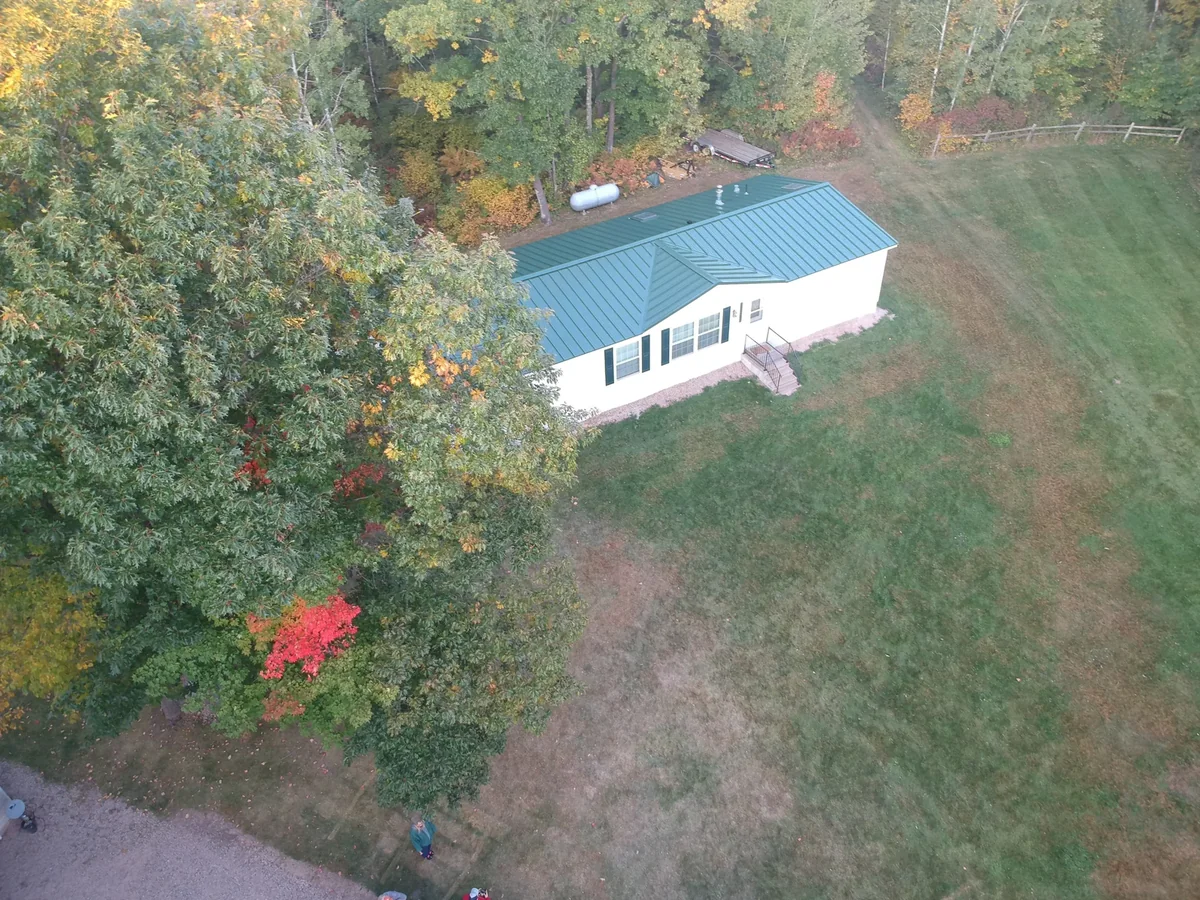 Elevated view of the green-roofed house surrounded by tall trees and lawn.