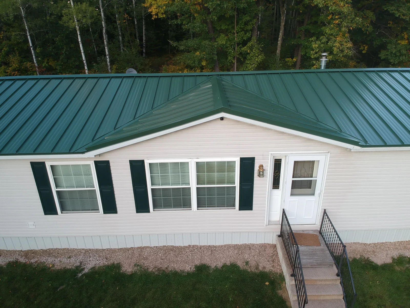 Front ground-level view of the home's entry below the green metal roof and dark shutters.