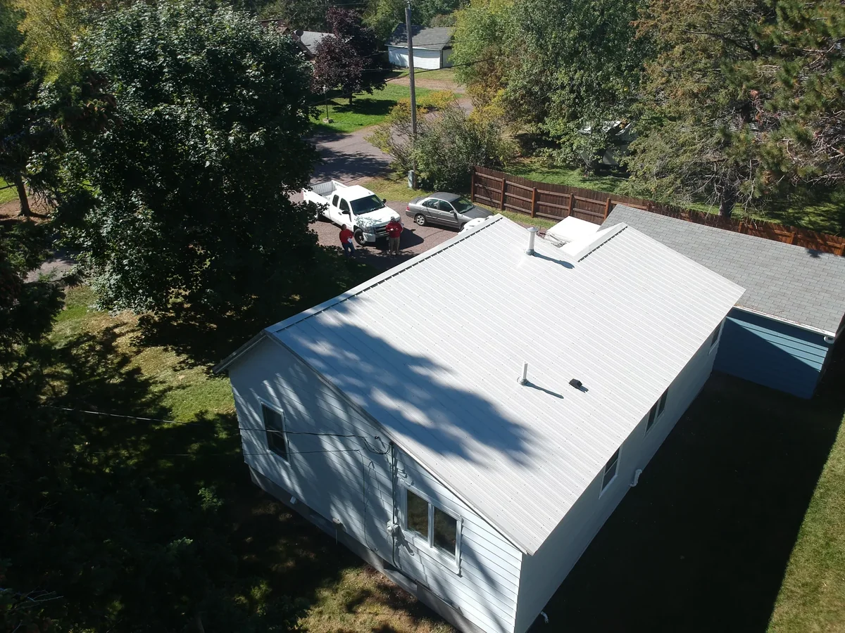 Aerial view of a white-sided home with a bright silver metal roof and shaded yard in Walker, MN