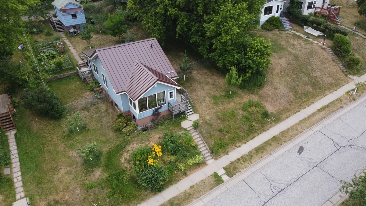 Aerial view of a light blue bungalow with a burgundy standing seam metal roof along a quiet street in Wayzata, MN