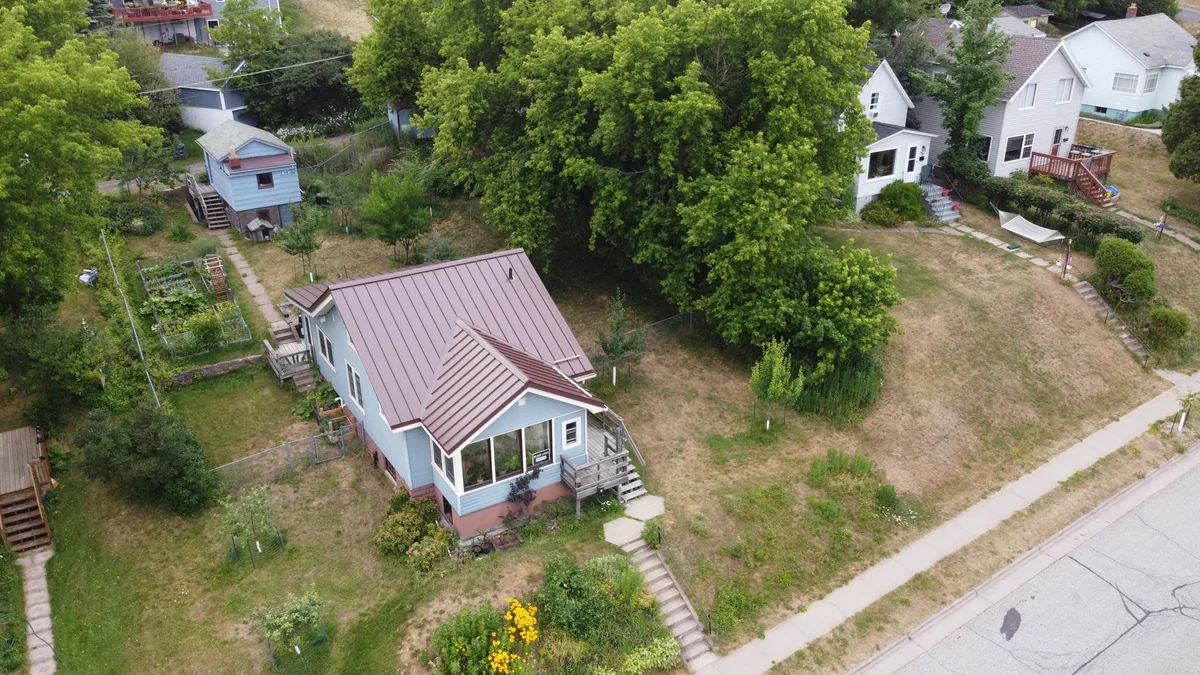 Side angle of the burgundy metal roof with the garden and neighboring homes